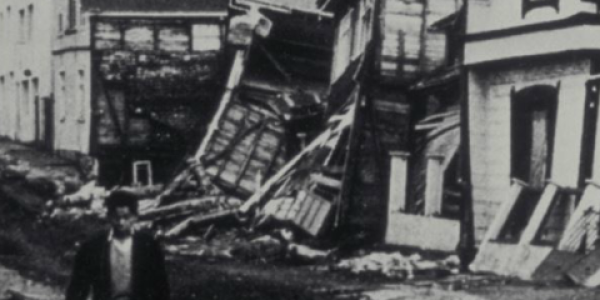 A black and white photo of a man walking past damaged homes in Valdivia, Chile caused by the 1960 Chilean Earthquake.