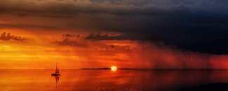 Photo of reddish sunset over ocean with sailboat Photo of reddish sunset over ocean with sailboat